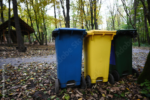 Three yellow, blue and green recycle bins in the autumn park on the ground.