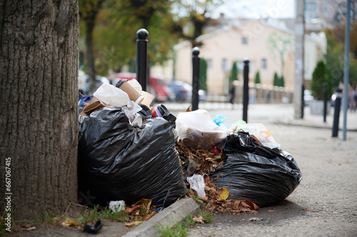 Garbage in bags on the street under a tree. The problem of ecology in the world. A carelessly throw away garbage bags on the street in the open photo