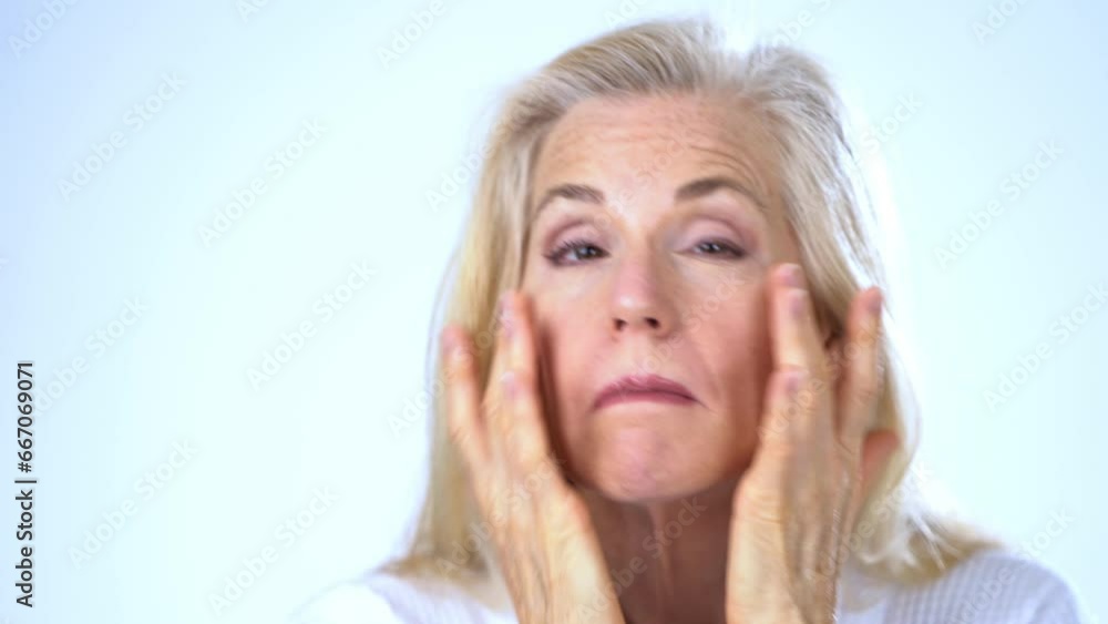 Mature middle-aged elderly woman model makeup hygienic looking at camera applying moisturizer face for skin care anti-aging cosmetic senior lady smiling on white studio background Mature middle-aged elderly woman model makeup hygienic looking at camera applying moisturizer face for skin care anti-aging cosmetic senior lady smiling on white studio background