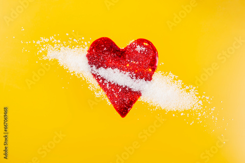 Red blood splatter in form of a heart mixed with sugar crystals on yellow background, soft focus close up, diabetes concept photo