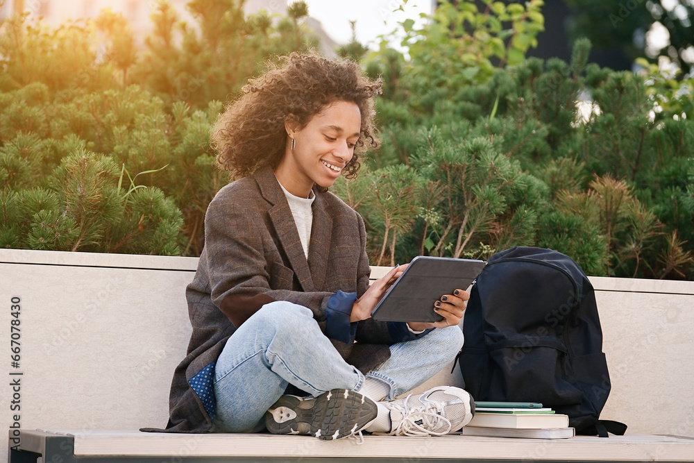 Young african american woman sitting on a bench and using tablet. People, friendship, studying, lifestyle concept    