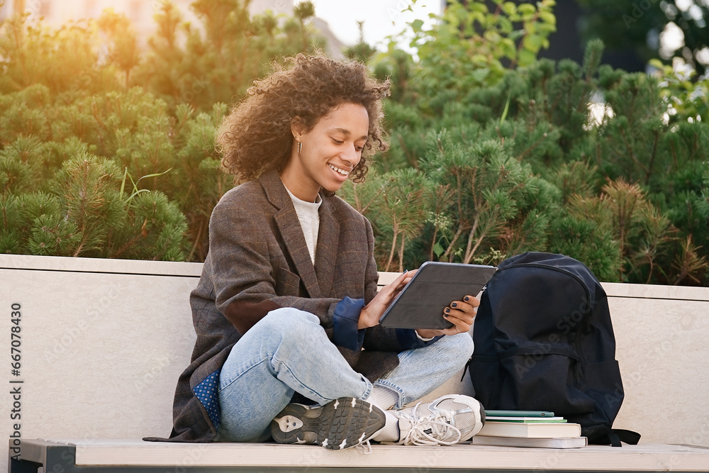 Young african american woman sitting on a bench and using tablet. People, friendship, studying, lifestyle concept Young african american woman sitting on a bench and using tablet. People, friendship, studying, lifestyle concept