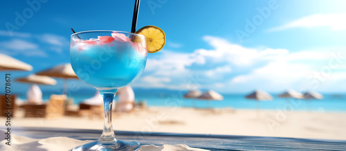 Blue Hawaii cocktail on a lagoon beach. A cocktail with lemon on the ocean beachfront. A beautiful glass with blue alcohol, a pipe and citrus in the sand. Blurred background of sea umbrellas & waves