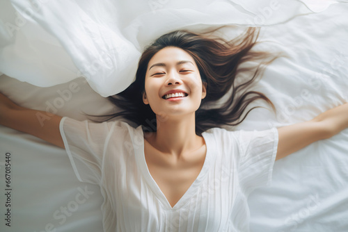 Young relaxed Asian woman resting in her bed with a smile. Top view