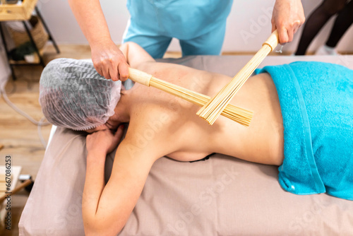 Close up of therapist hands massaging female legs with bamboo stick. © яна винникова
