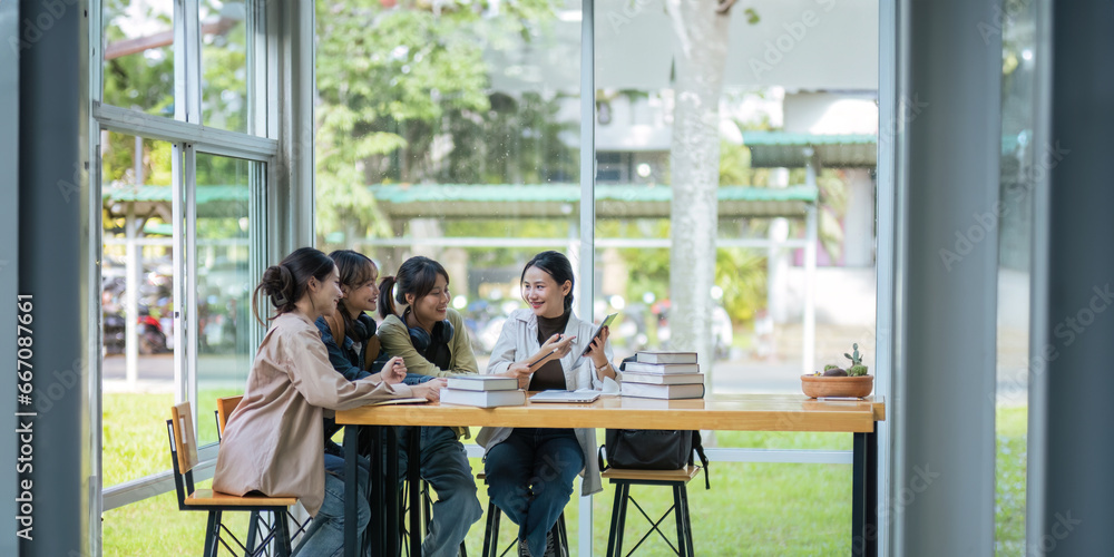 University students sitting together at table with book and laptop. Happy young people doing group study in college campus College and University life concept University students sitting together at table with book and laptop. Happy young people doing group study in college campus College and University life concept