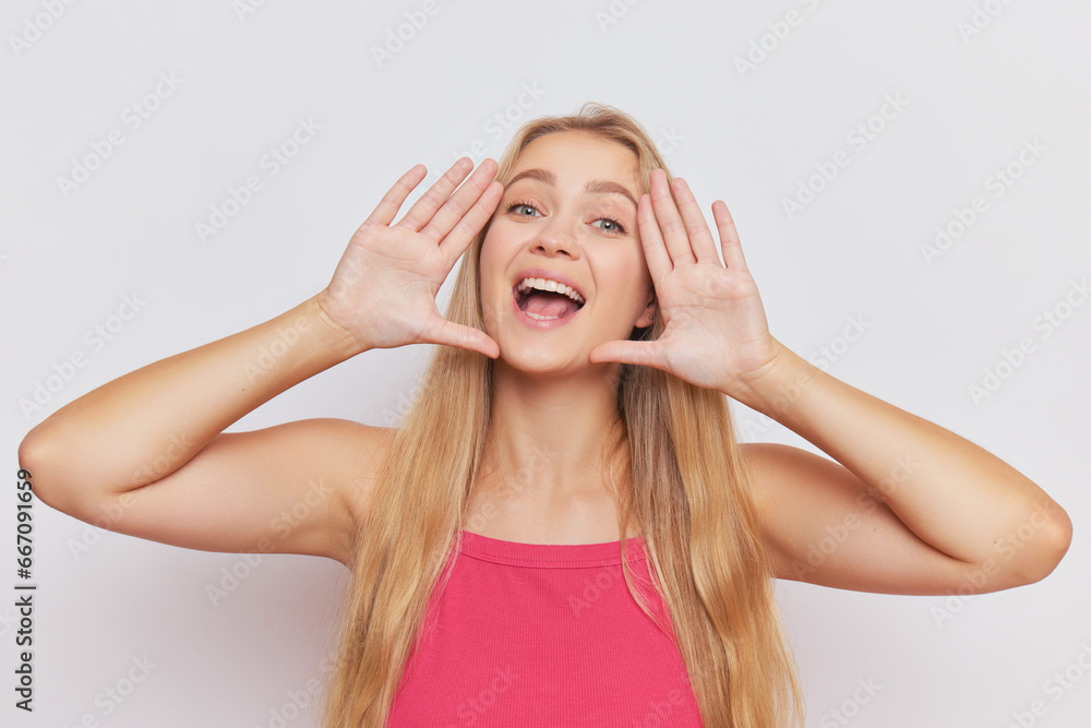 Pretty blonde girl with long hair wearing pink top poses on background holding her handsat her face, wonderful life concept, copy space Pretty blonde girl with long hair wearing pink top poses on background holding her handsat her face, wonderful life concept, copy space