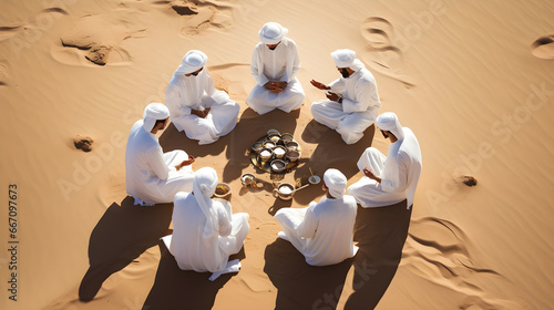 Muslim men in white traditional clothes who drink coffee or tee and enjoys calm morning in midst of endless sandy desert with pure white sand in open air, top view photo