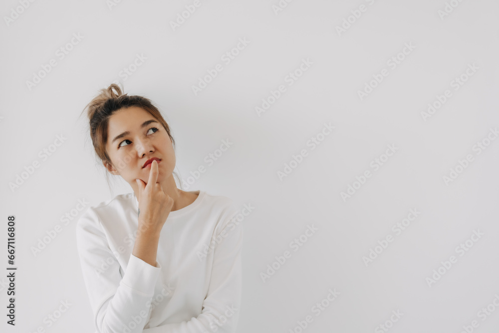 Asian Thai woman wear sweater bun hair, touching chin and mouth with doubt and curious face, have question thinking and looking at empty space, isolated on white background wall at winter. Asian Thai woman wear sweater bun hair, touching chin and mouth with doubt and curious face, have question thinking and looking at empty space, isolated on white background wall at winter.