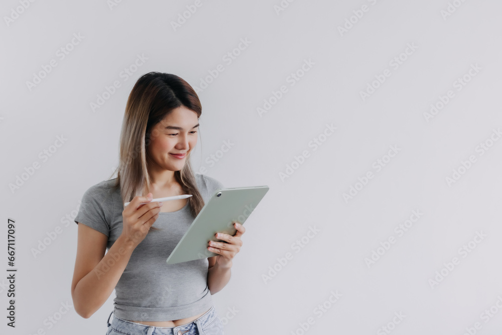 Asian Thai woman wear grey, hands holding tablet and white pen, have good idea with smiling face while working and looking at computer, isolated on white background. Asian Thai woman wear grey, hands holding tablet and white pen, have good idea with smiling face while working and looking at computer, isolated on white background.