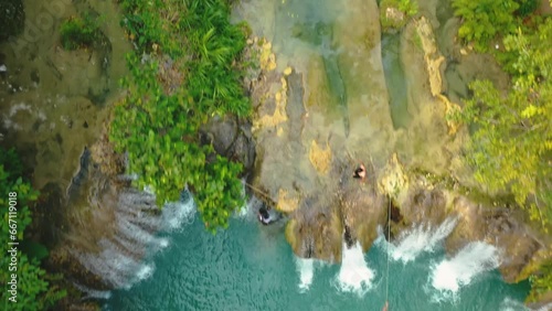 Cambugahay falls, Siquijor island, Philippines. Aerial backward travelling. Cinematic drone view. Filipino tourists swimming in the turquoise waterfall. Famous travel destination. photo