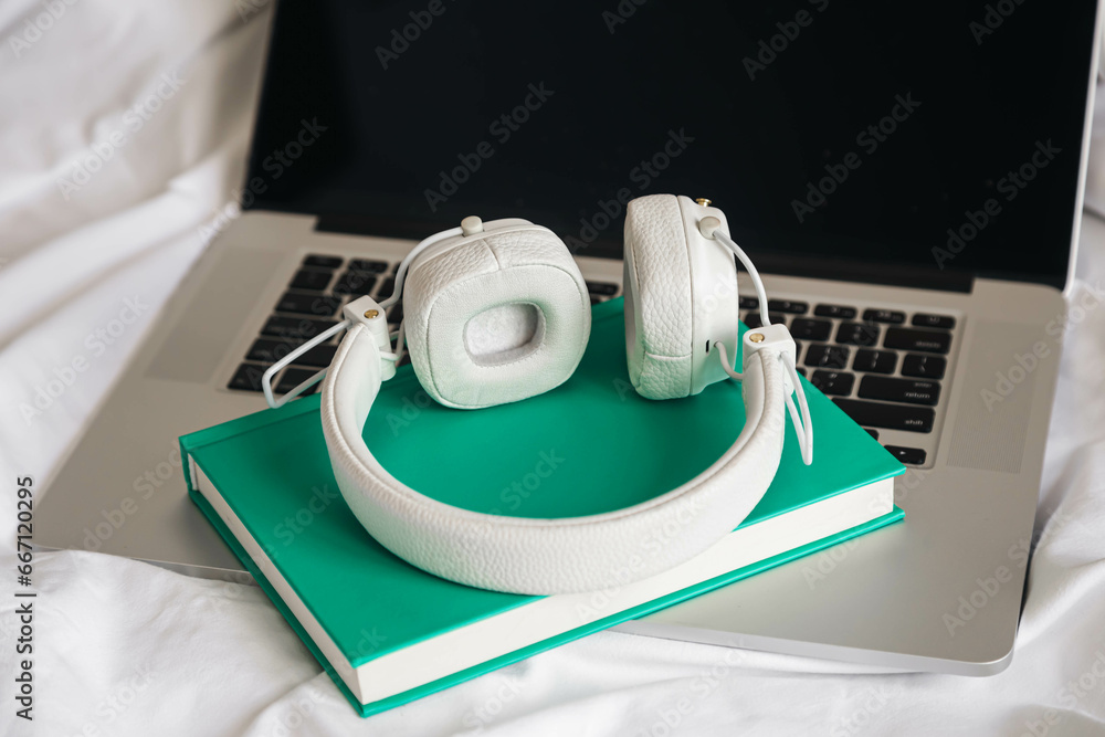 White headphones, book and laptop in a white bed, hobby, work at home, lazy day off.