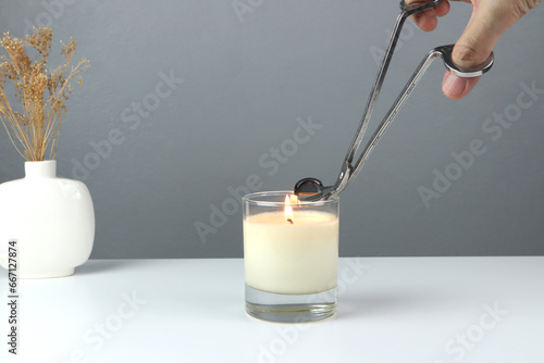 Fotografija nice scented candle on the white table is cut the wick by silver stainless steel