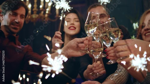 Excited group of European friends in front of the camera cheers with the champagne glasses holding the sparkles on hands smiling large they celebrating the Christmas or New Year together they are