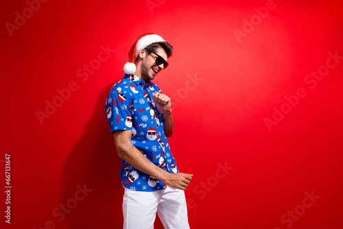 Photo of carefree guy wear santa hat with blue stylish shirt dance traditional christmas time night party isolated on red color background © deagreez