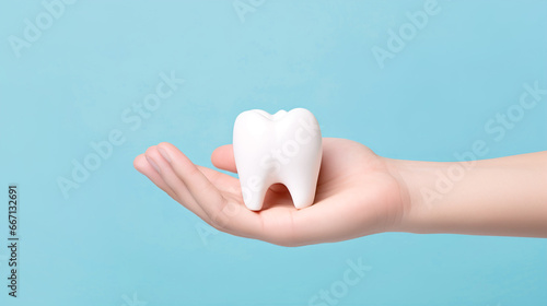 Hand holding a tooth close-up on a blue background with copyspace. Dental clinic concept for dental treatment