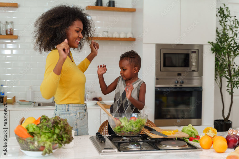 Happy African mother and son making salad while preparing food in the kitchen having fun, mother and son cooking activity concept. - obrazy, fototapety, plakaty 