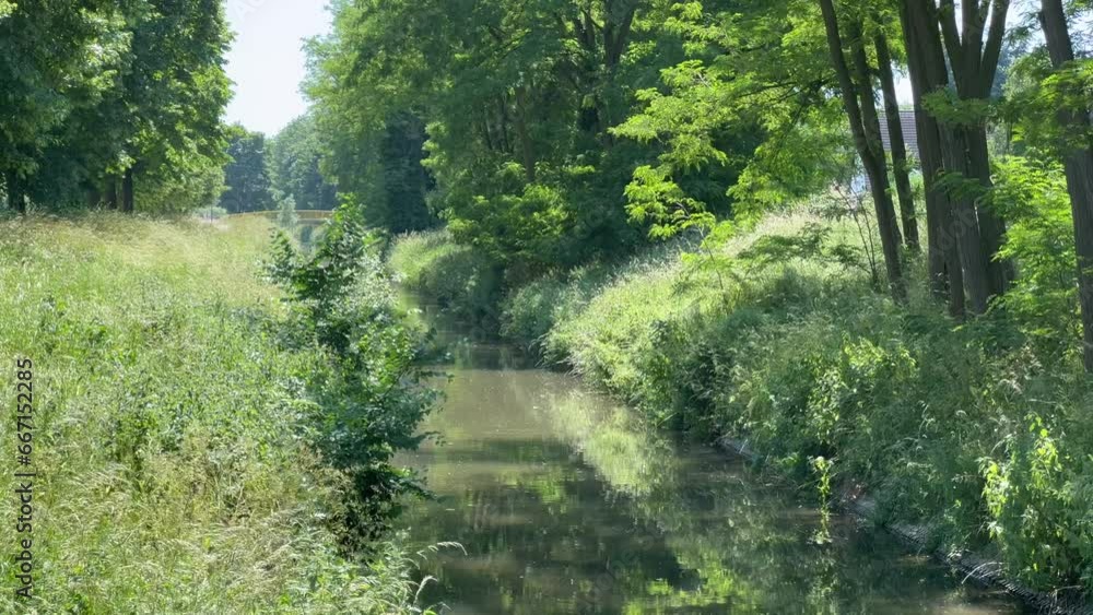 Ruhiger trüber Fluss fließt langsam durch ein grünes Idyll an einem sonnigen Tag mit gelber Brücke im Hintergrund Ruhiger trüber Fluss fließt langsam durch ein grünes Idyll an einem sonnigen Tag mit gelber Brücke im Hintergrund