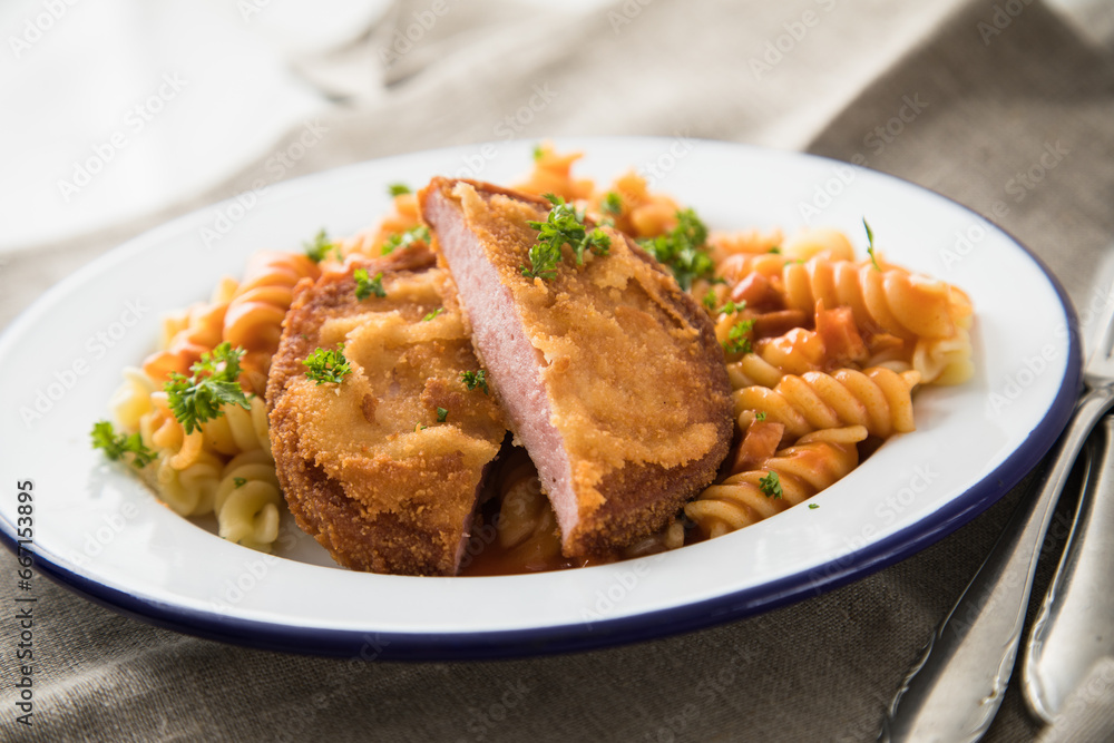 Jägerschnitzel nach DDR GDR Rezept mit Jagdwurst paniert, Spirelli Fusilli Nudeln, Tomatensoße, Petersilie auf Emaille Teller, Besteck und grauer Leinen Serviette Jägerschnitzel nach DDR GDR Rezept mit Jagdwurst paniert, Spirelli Fusilli Nudeln, Tomatensoße, Petersilie auf Emaille Teller, Besteck und grauer Leinen Serviette
