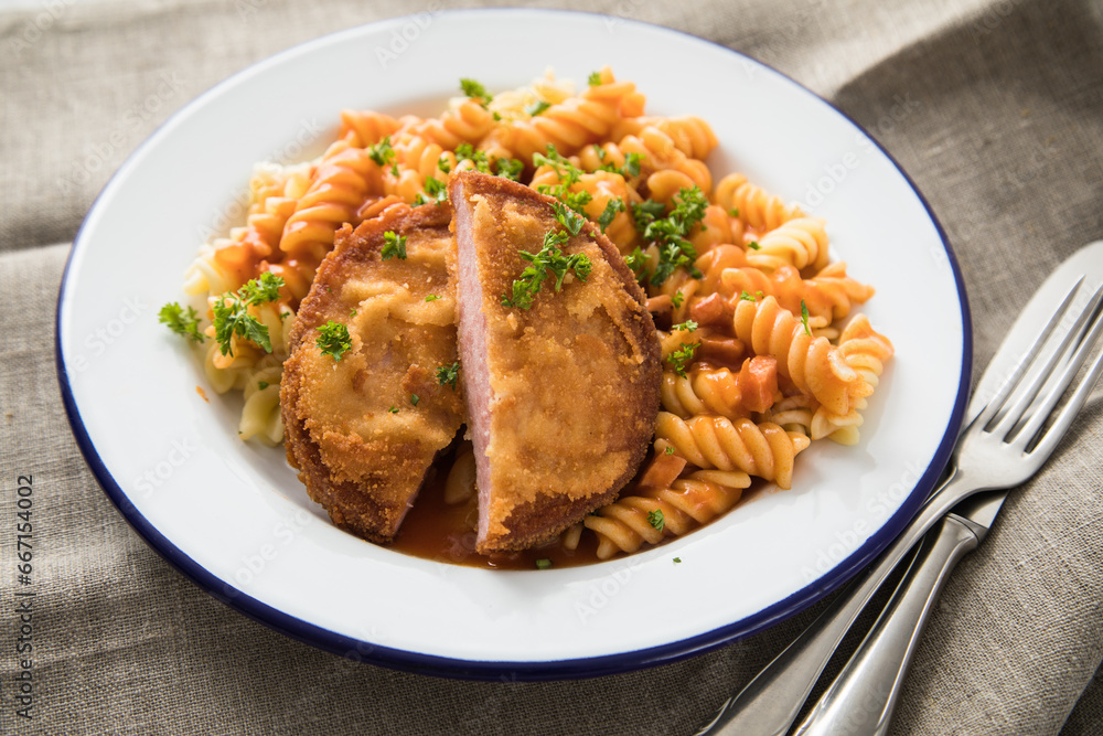 Jägerschnitzel nach DDR GDR Rezept mit Jagdwurst paniert, Spirelli Fusilli Nudeln, Tomatensoße, Petersilie auf Emaille Teller, Besteck und grauer Leinen Serviette Jägerschnitzel nach DDR GDR Rezept mit Jagdwurst paniert, Spirelli Fusilli Nudeln, Tomatensoße, Petersilie auf Emaille Teller, Besteck und grauer Leinen Serviette