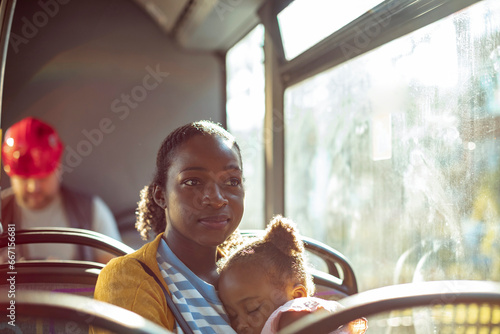 Loving young mother holding her sleepy daughter while riding the bus photo