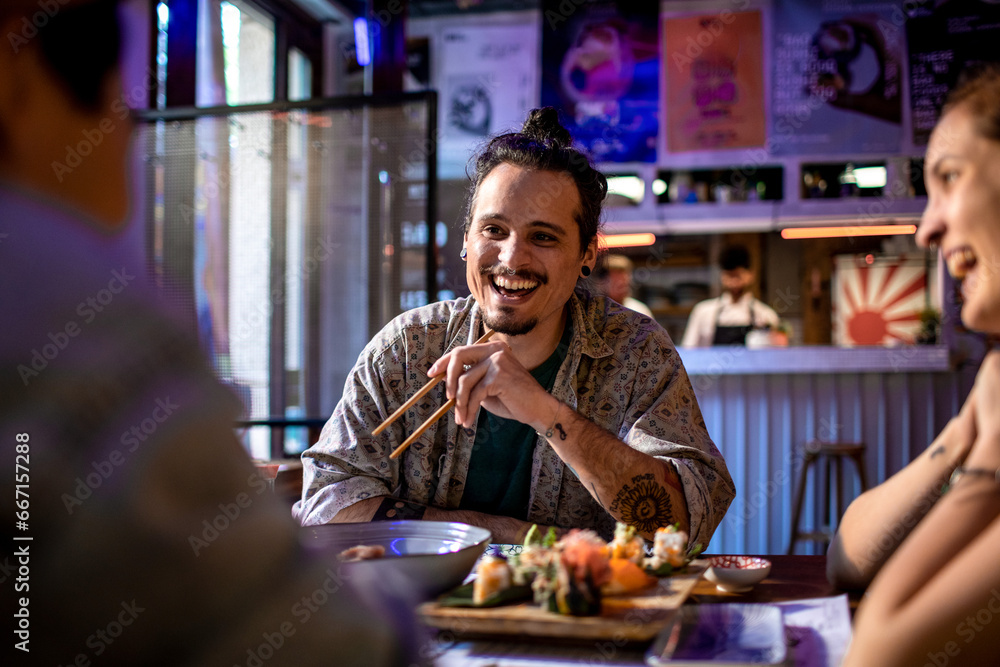 Happy young man eating sushi with his friends in a restaurant Happy young man eating sushi with his friends in a restaurant