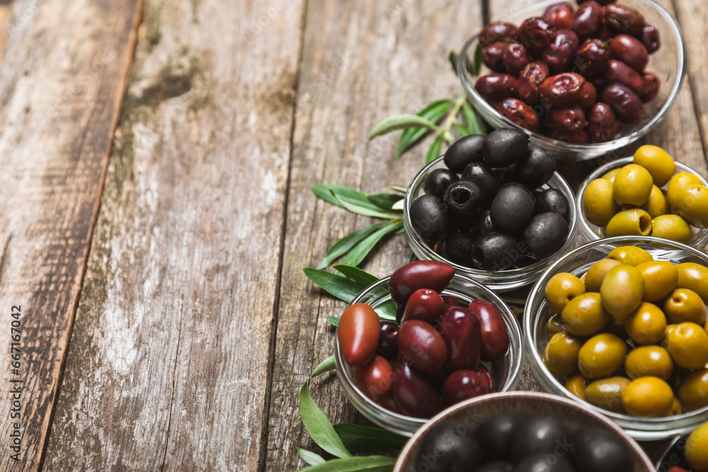 A set of green, red and black olives on background. Various types of olives in bowls and fresh olive leaves. Vegan. Olive fruits. Place for text. Copy space A set of green, red and black olives on background. Various types of olives in bowls and fresh olive leaves. Vegan. Olive fruits. Place for text. Copy space