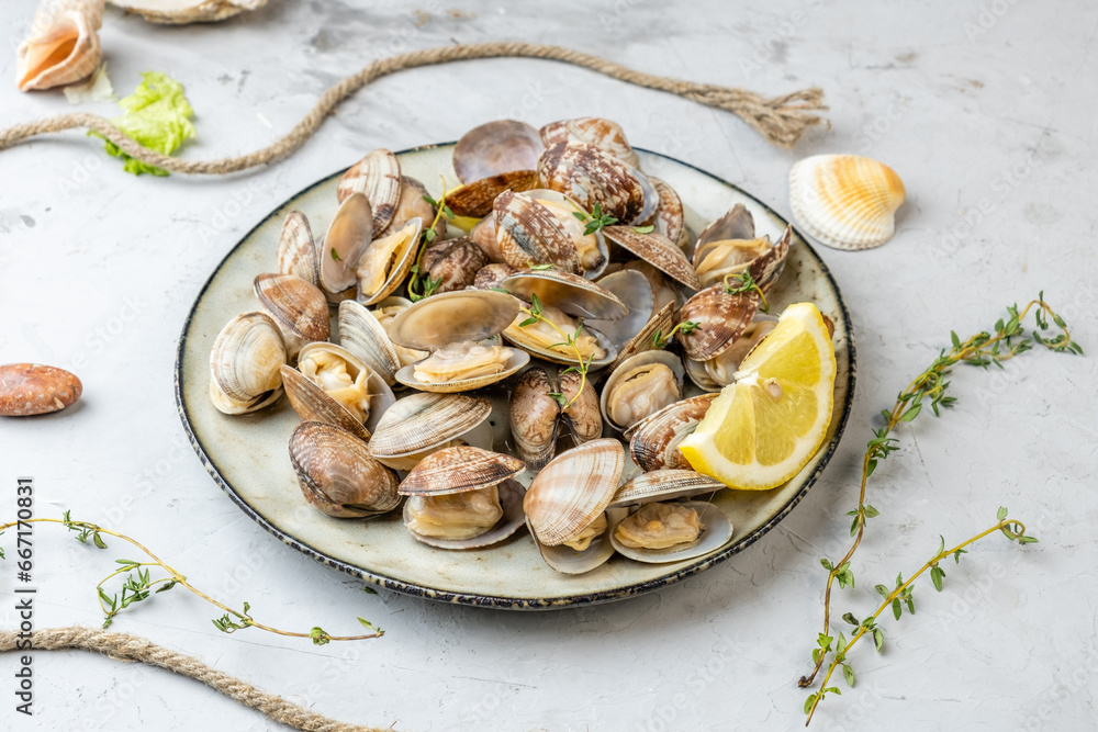 Vongole shells cooked, with lemon and herbs in a plate on a light background