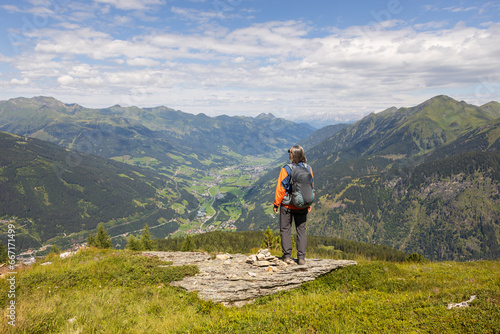 Gray-haired long-haired male hiker with backpack standing at the edge of cliff and looking at a mountain valley  Austria