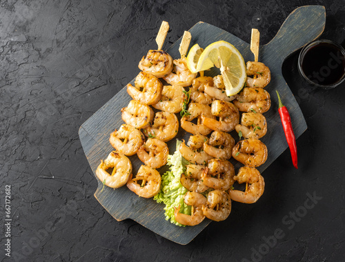 Skewers with grilled shrimp meat, dark background, serving board.