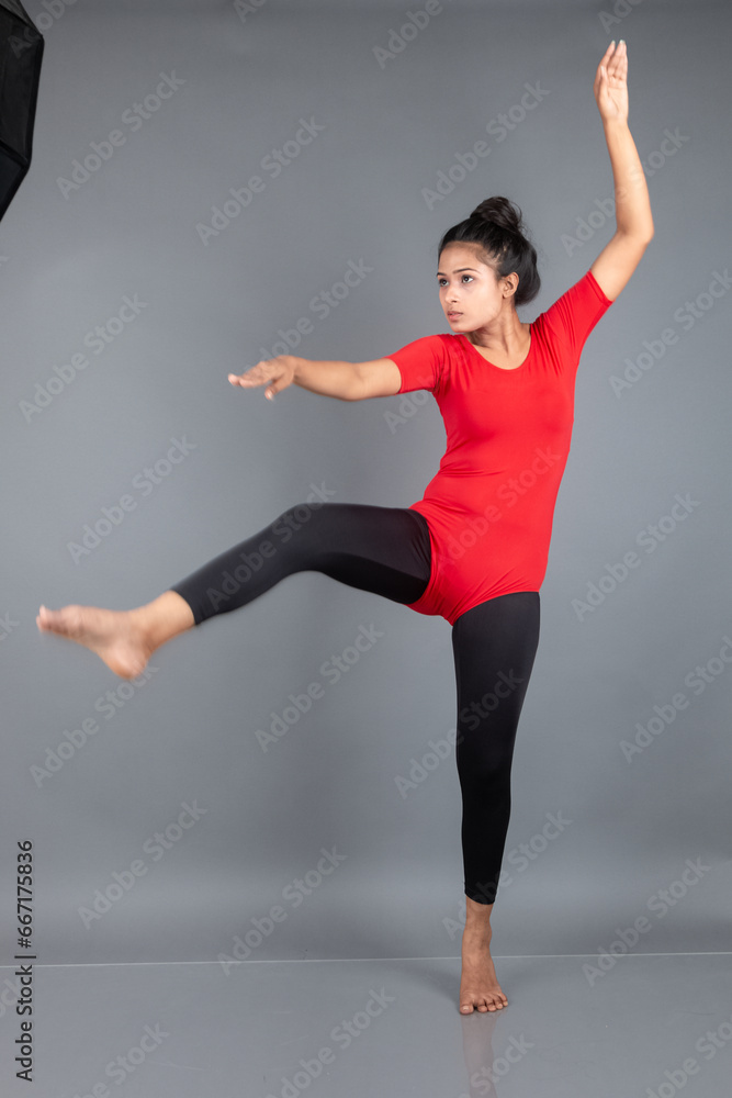 Obraz premium Healthy young woman in red t-shirt and black leggings doing yoga and stretching exercises isolated on grey background