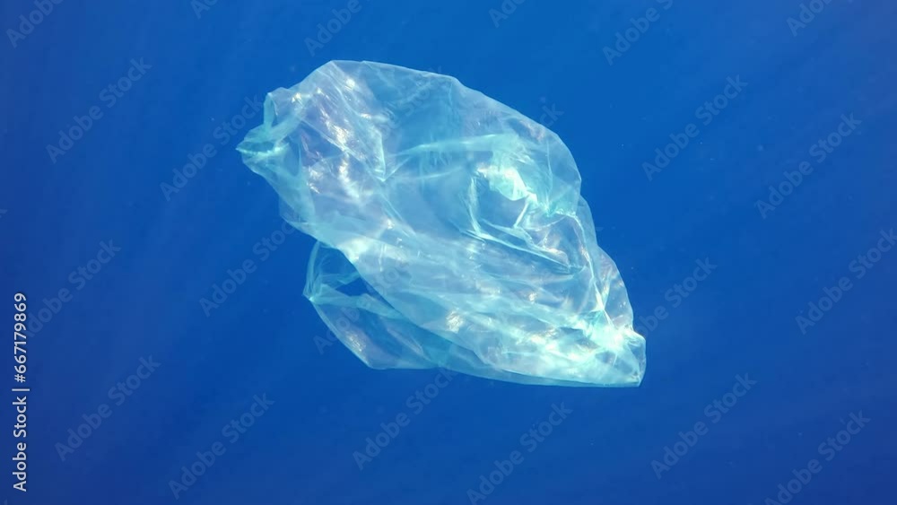 Disposable white plastic bag slowly sinks into blue abyss in bright rays of sun. Plastic bag floating underwater in clear blue sea. Plastic pollution of Ocean Disposable white plastic bag slowly sinks into blue abyss in bright rays of sun. Plastic bag floating underwater in clear blue sea. Plastic pollution of Ocean