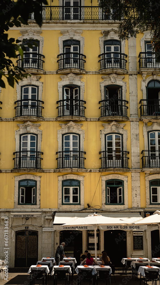 Lisbon, Portugal - May 25, 2023: Facade of a yellow building with a restaurant and the esplanade on the ground floor