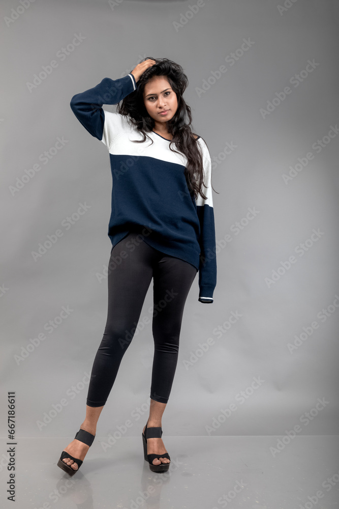 Indian young female model in casual winterwear against grey background. Long black haired model wearing black leggings, blue and white sweatshirt. Indian young female model in casual winterwear against grey background. Long black haired model wearing black leggings, blue and white sweatshirt.
