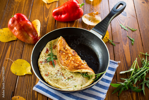 Fried omelets with various autumn vegetables in a frying pan on a wooden table.