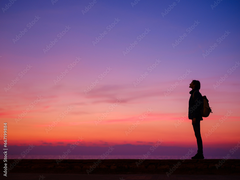 Woman tourist against colorful sunset sky. Travel, tourism concept. Active lifestyle.