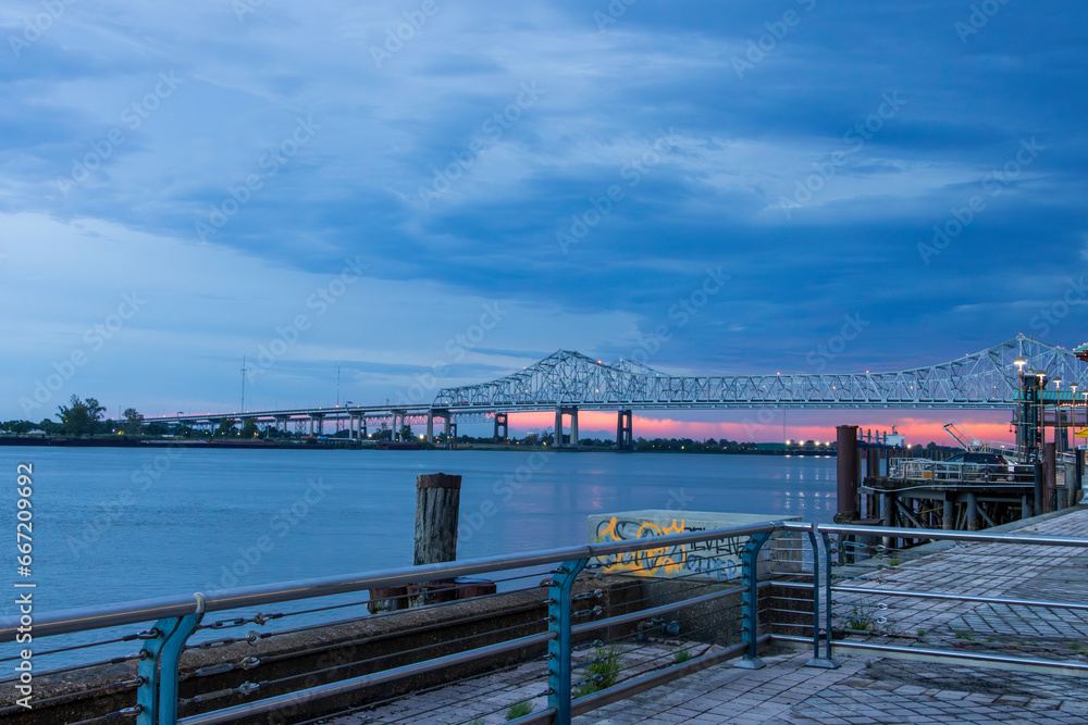 a gorgeous summer landscape along the Mississippi River with the Crescent City Connection bridge over the water with blue sky and powerful clouds at sunset in New Orleans Louisiana USA