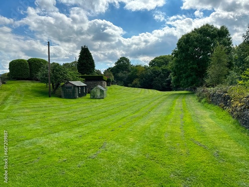 Freshly mown grassland, with a wooden shed, a greenhouse, dry stone walls, and old trees near, Keighley, UK photo