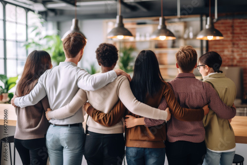 Group of mix race people, co-workers hugging each other at the work place supporting each other, back view. Unity, togetherness, straight and LGBTQ people working together