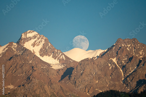 A mountain landscape with an almost full moon. Komsomol Peak (Nursultan) and Karlytau peak. The Alatau Ridge on the Tien Shan. Almaty, Kazakhstan photo