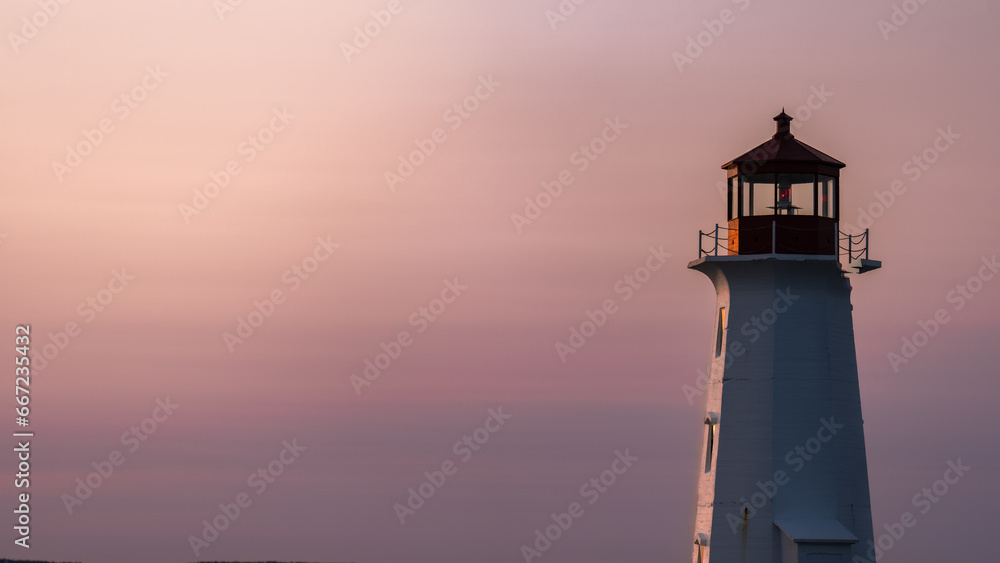 Close-up of a red and white lighthouse as the sun sets. A luminous pink atmosphere