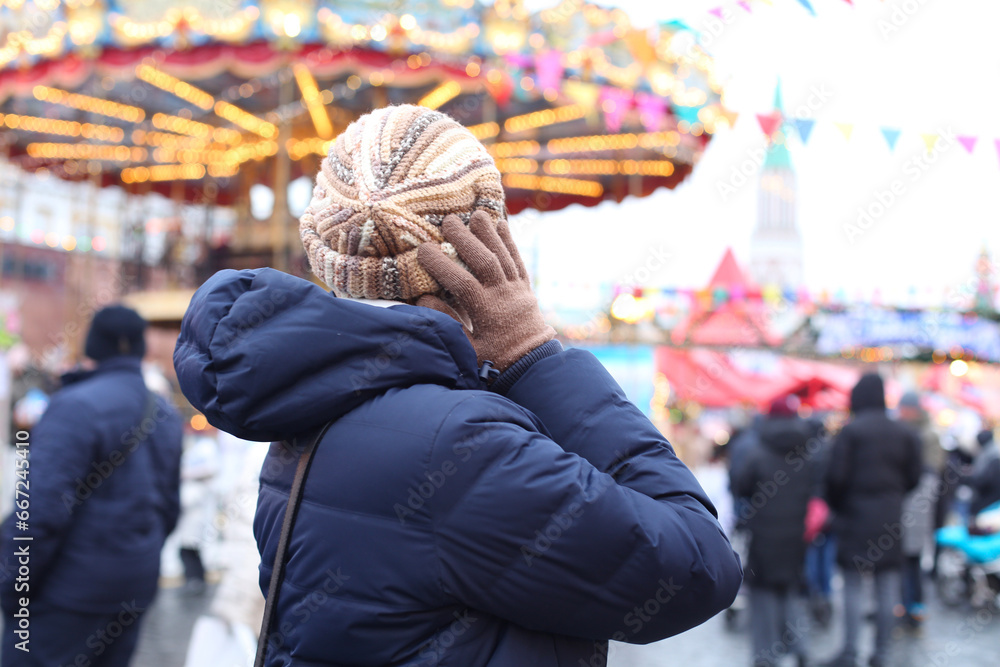 Unrecognizable woman in a hat looks at a Christmas carousel at a fair, winter