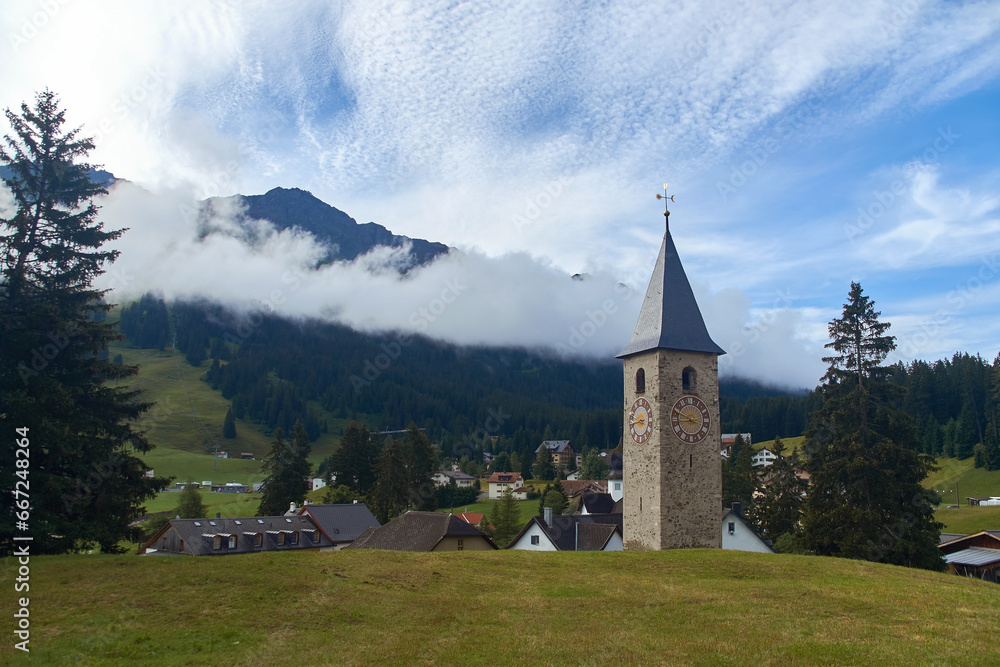 Beautiful swiss alpine countryside with a medieval bell tower with a clock and Rothorn mountain on background in Churwalden village in Switzerland formerly Parpan