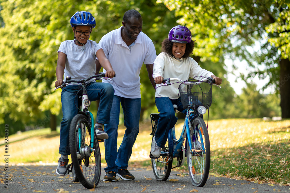 Fototapeta premium Father teaching his kids riding a bike and looking happy