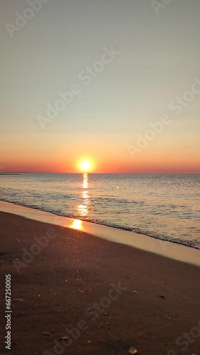 Beautiful sunrise on sea coast seaside. Sun rising from clouds in sky on blue sea with sea waves rolling on sandy beach. Bright shining sun. Seascape sea landscape. Natural nature background Vertical