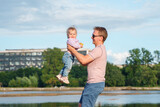 Joyful kid baby plays with father on the shore of the lake in the evening. The concept of a happy family and childhood, father support