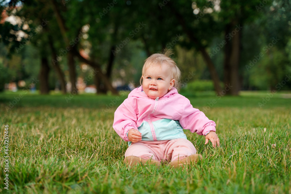 Cute caucasian kid baby sitting on the grass in a jacket Cute caucasian kid baby sitting on the grass in a jacket