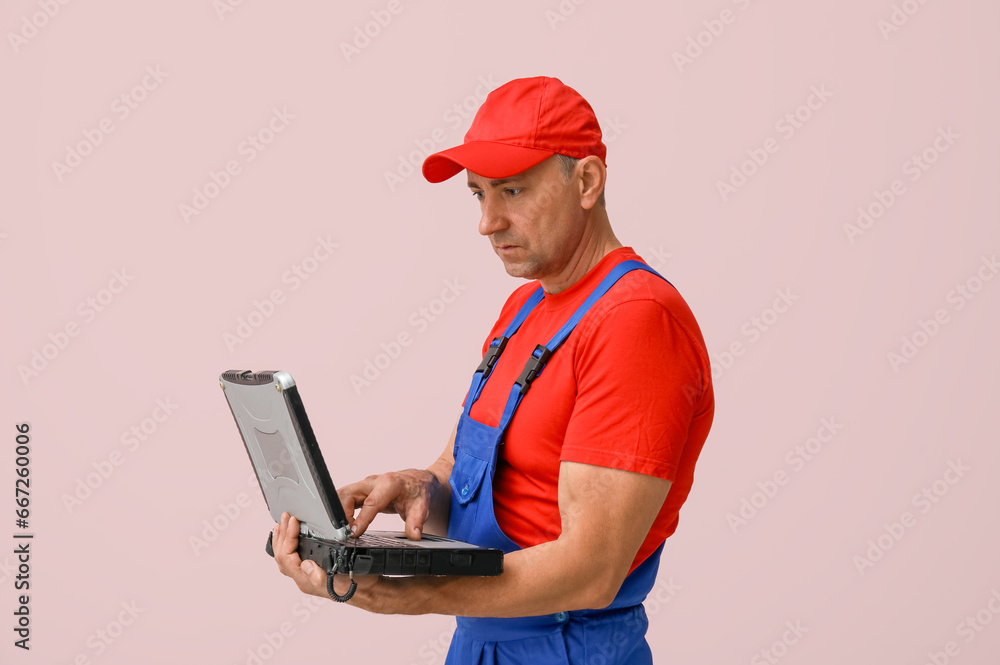 Portrait of male mechanic with old laptop on pink background Portrait of male mechanic with old laptop on pink background