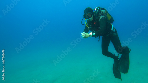 Male diver standing alone standing underwater, hands clasped surrounded by clean blue. Space for text, advertisement