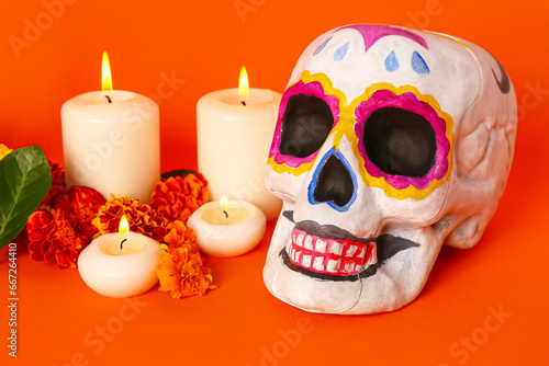 Painted skull with marigold flowers and candles on orange background. Celebration of Mexico's Day of the Dead (El Dia de Muertos)